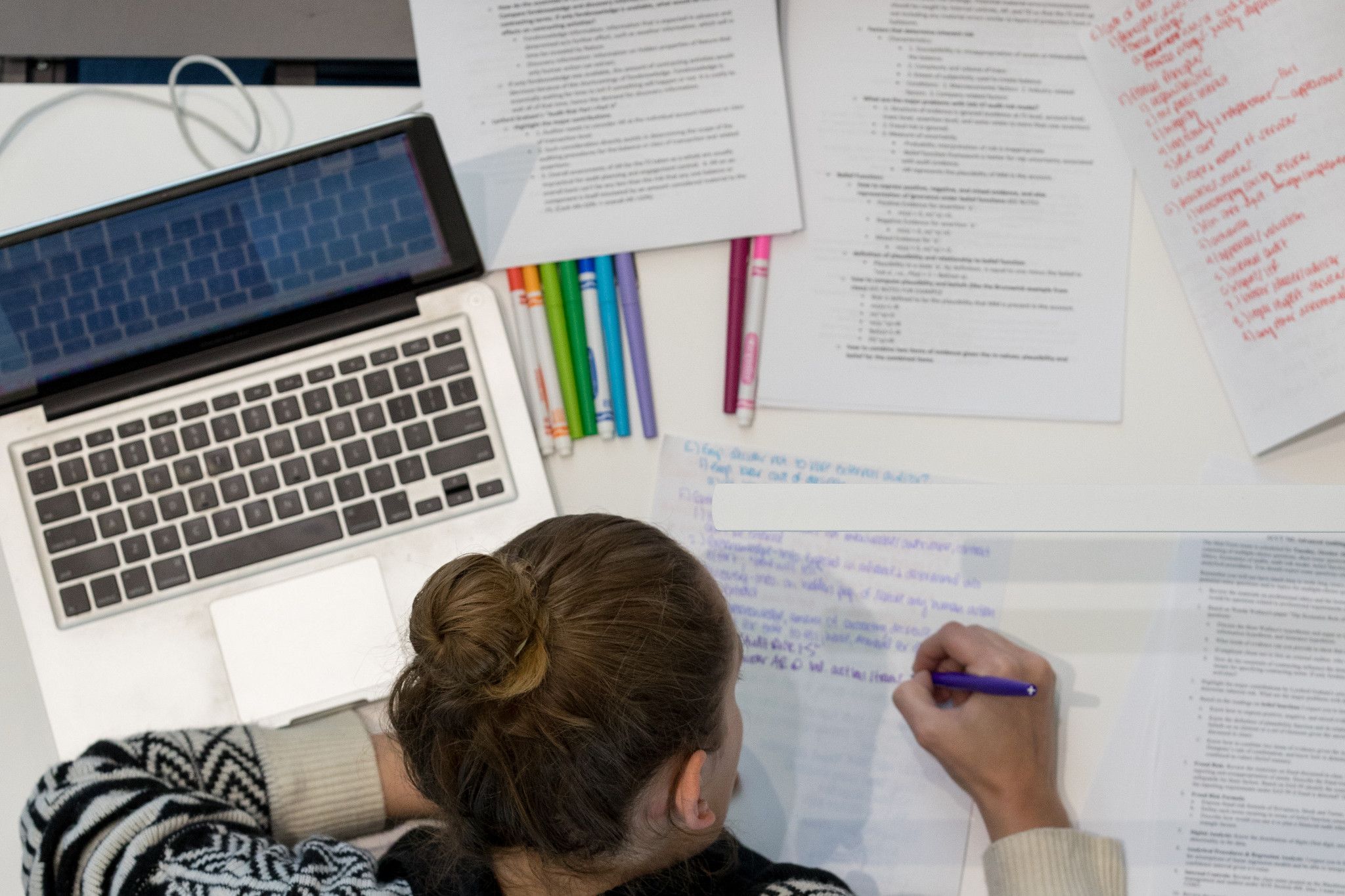Birds-eye view of student writing notes on many sheets of paper
