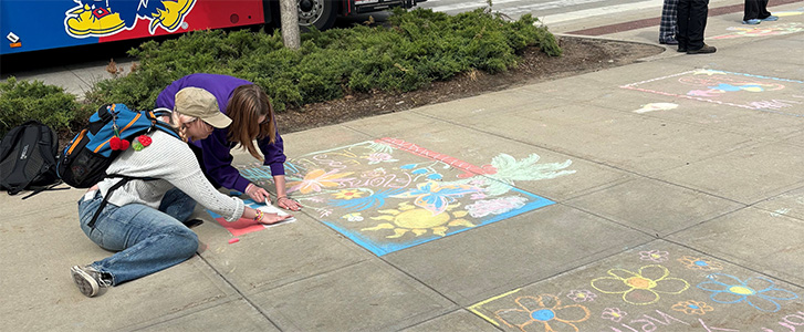 Two students drawing chalk on Wescoe Beach