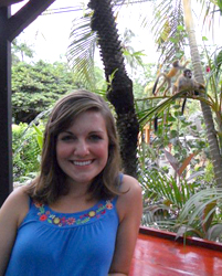 Meir posing in front of a forest. A monkey is on a tree in the background