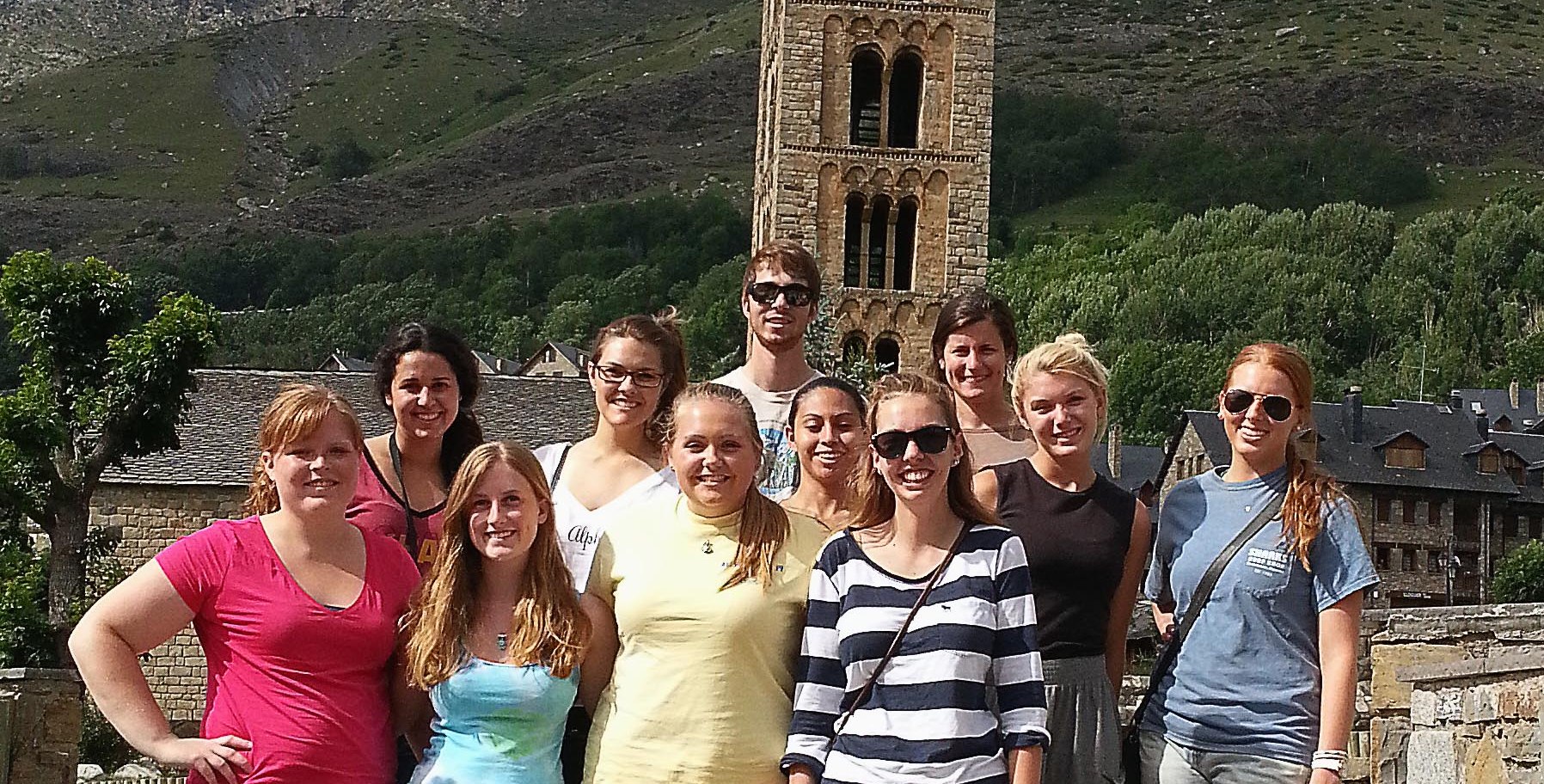 Photo of a group of KU students on a study abroad trip. There is a large brick building in the background surrounded by green hills.